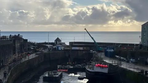 Charlestown Harbour lock gate. There is a crane over the area. The sea is in the background.