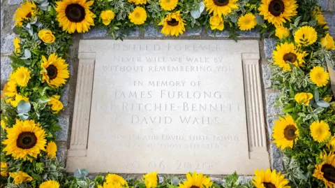Reading Borough Council The permanent memorial stone to Mr Furlong, Mr Ritchie-Bennett and Mr Wails in Forbury Gardens has a sunflowers wreath all around it.