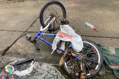 An old blue and white mountain bike is among the junk found along Willow Brook and as seen here plastic bags and old clothes are caught up in it. 