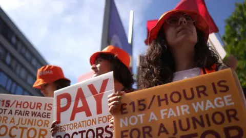 A trio of women hold signs that read Pay Restoration for Doctors