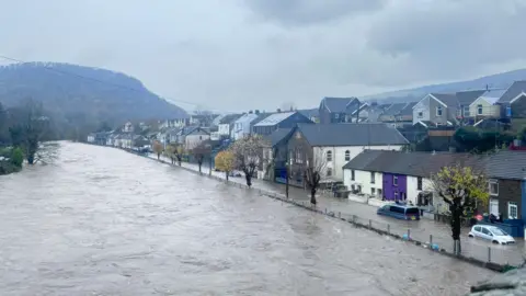 BBC Weather Watchers / Emma Wide image of River Taff in Pontypridd, showing the river having burst its banks. Floodwater can be seen in a street directly to its right, submerging cars in water.