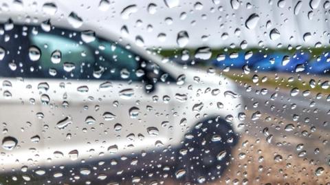 A white car seen blurrily through raindrop-spattered glass