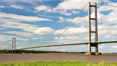 Steve Goacher/Getty A large bridge stretching across a long body of water. There is a blue sky and white clouds.