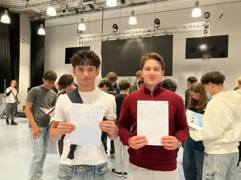 Two boys hold their GCSE results