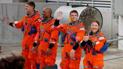Reuters The four astronauts in their bright orange space suits waving before they get into the capsule.