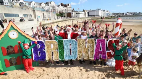 East Riding of Yorkshire Council Beachgoers stand in the sand and cheer with a glittery 'Bridmas' sign, with elves and Father Christmas joining in the celebration.