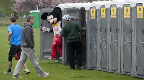 Getty Images Fun runners at the start of the Virgin London Marathon - a man dressed in a Mickey Mouse costumes exiting a portable toilet
