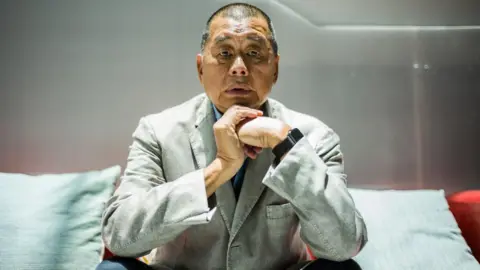 Getty Images Jimmy Lai, in a gray suit and black pants, poses for a photograph during an interview with AFP news agency in Hong Kong