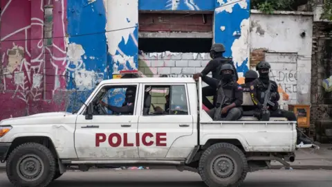 EPA A police vehicle with armed officers sitting in the back patrols a street after attack on a public hospital in Port-au-Prince, Haiti, 24 December 2024. 