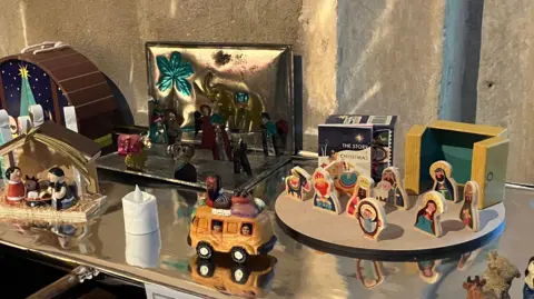 A view of a few different small nativity scenes today - one is wooden and child-like, another in a yellow VW camper van. One at the back is metallic-like, with an elephant featuring. Another a simple style and includes a stable structure.