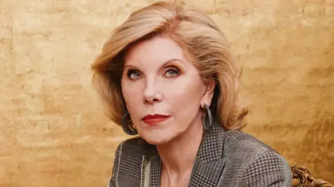 Emilio Madrid Christine Baranski sitting in front of a gold background