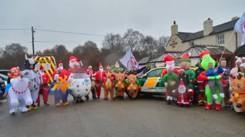 Staffordshire Birdseye Photography A large group of people dressed in a variety of inflatable Christmas costumes standing in a road with ambulance vehicles parked behind them