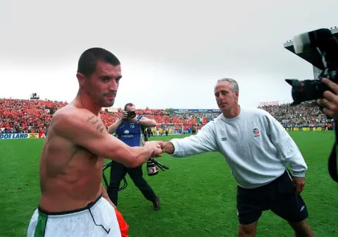 Lorraine O'Sullivan/INPHO via Getty Images Roy Keane, on the pitch at Lansdowne Road, with his top off,  shaking hands with manager Mick McCarthy, who is wearing a sweatshirt and shorts.