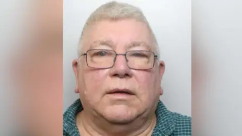 National Crime Agency A mugshot of David Saynor who has a round face, square glasses and short grey hair. He has no facial hair.