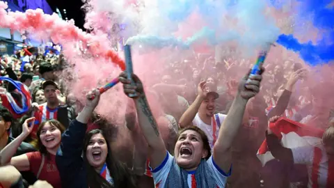 A woman holiding up two flares in the street as the citizens of Asunscion party hard following Paraguay's victory against Germany