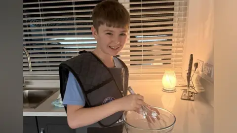 Harvey, 12, standing in the kitchen holding a mixing bowl and whisk and looking into the camera smiling.