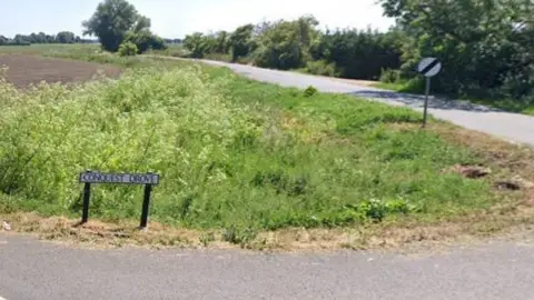 Google Conquest Drove at the corner with Straight Drove. A white road sign saying Conquest Drove in black letters edges a verge. The single-track road is behind it, with a 60mph sign.