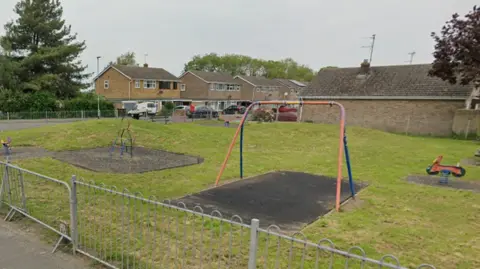 Google shot of Fern Park play area on Pinchbeck Road in Spalding. It is a lawned area with various apparatus, sone of which appears to be out of order. 