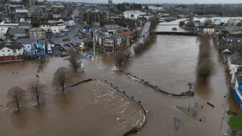 Niall Carson/PA Wire An aerial view of the Enniscorthy, County Wexford, where the River Slaney bursts its banks. Brown floodwater is covering a road bridge and streets along the quay. Several buildings lining the quays are sitting in water. 