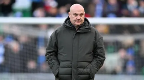 Richard Hill walking on the pitch in 2024 at an FA Cup game with his hands in his coat pockets