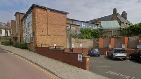 Google A brown building with a car park next to it.
