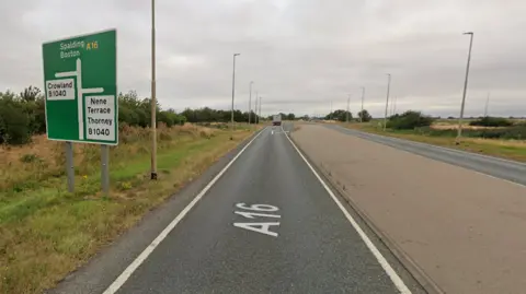 A section of the A16. A green sign is to the left, directing towards Spalding and Boston straight ahead. Street lights are lined either side of the road with grass verges. 