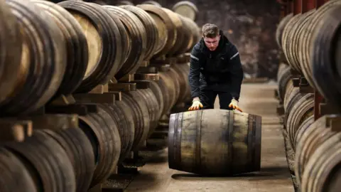 A man rolling a Scottish whisky barrel in a distillery warehouse