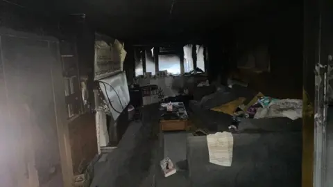 Jamie Warden/Electrical Safety First A living room that has been destroyed in a fire. There is black soot all over the room and items have been burnt in the fire. 