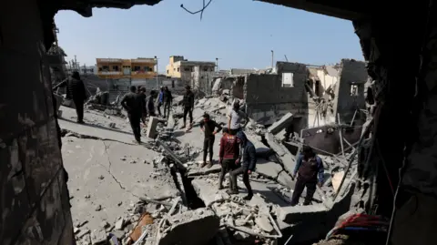 Reuters Palestinians inspect the rubble and destruction of what used to be a home after Monday night's airstrikes by Israel's military - seen through a large hole in a building