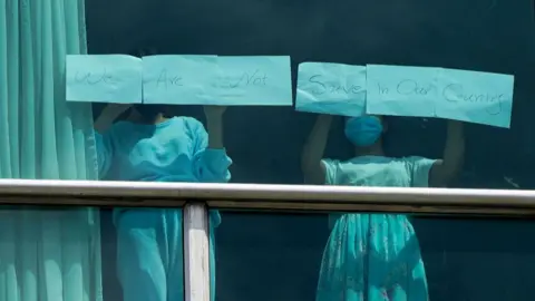 Migrants deported from the US to Panama stand at a hotel window holding up paper with the words "We Are Not Save In Our Country".