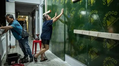 Getty Images Restaurant workers board up a restaurant ahead of the arrival of the forecasted Super Typhoon Bavi in Guam on July 4, 2026. People in Guam and the Northern Marianas readied themselves on July 4 as the second "super typhoon" to threaten the US Pacific territories since April drew closer, bringing the equivalent of category-5 hurricane winds. (
