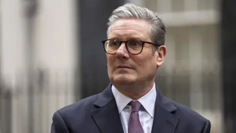 PA Media Starmer, seen from the shoulders up wearing glasses and a navy suit with purple patterned tie, looks to the left