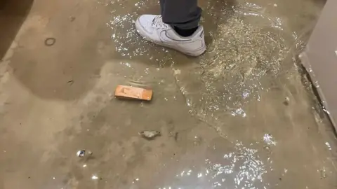 Stewart Bell A flooded floor. The foot of a man standing in the water is visible, showing how high the water has risen. 