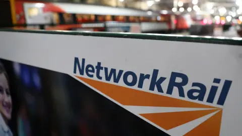 Generic image of a Network Rail sign in bold blue writing with blurred trains in the background. 