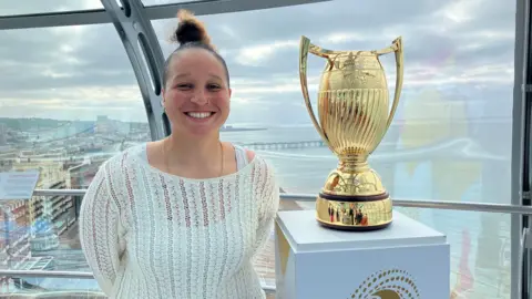 Sam Dixon-French/BBC Ex England rugby international Shaunagh Brown with the world cup trophy at the top of Brighton i360 with a view of Brighton behind