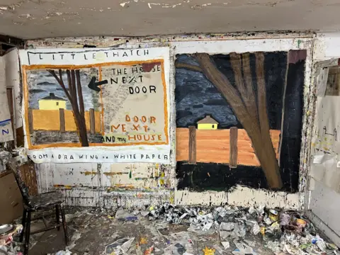 Painting showing on left -- yellow house behind brown fence and big tree
on the right -- tree prominent and dark sky, smaller house
and the frame looking like a meat cleaver with the words Little Thatch & The House Next door