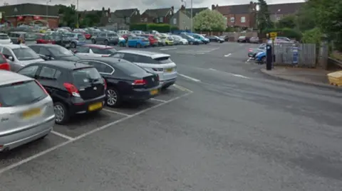 Google A full car park filled with cars, with a parking machine to the right of the image