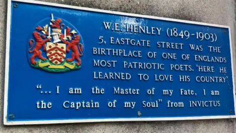 A blue plaque marking the birthplace of WE Henley in Gloucester. It has white text on the blue background. It contains the text "I am the master of my fate, I am the captain of my soul"
