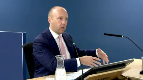 Matt Hancock wearing a blue suit and a light pink tie, sitting at a lectern at the Covid Inquiry on Wednesday. 