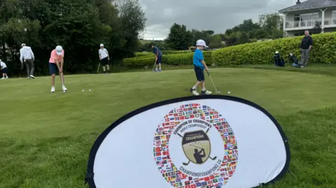 Young golfers practise putting in front of tournament crest