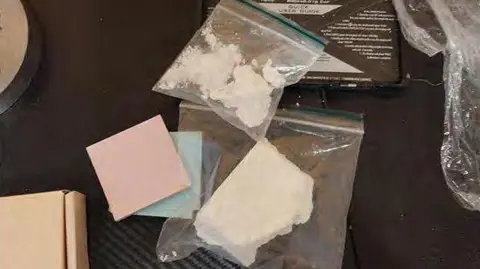 Essex Police Two clear bags of white class A drugs are placed on a black surface close to a cardboard box and pink and blue sticky notepaper.
