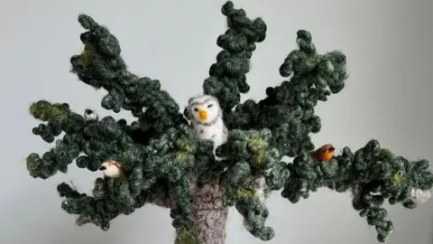 Mandy Smith/needlefeltingnook A needle felted tree with leaf-covered branches and birds and an owl sitting among the foliage.