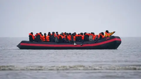 PA Media A group of of around 30 people wearing orange life jackets crammed onto a small boat in the English Channel