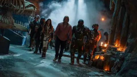 Giles Keyte, Amazon MGM Studios 2026 A still from Masters of the Universe. A group of characters walk towards the camera in a dark cave-like environment. There are candles and mist around them.