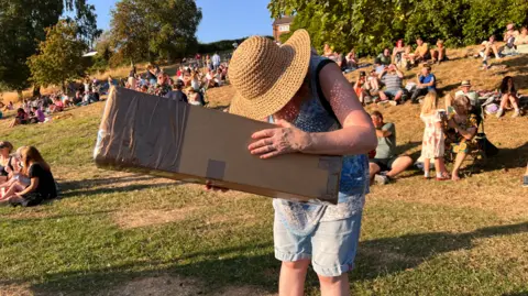 A woman is looking through a hole in a giant cardboard box at the sun