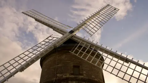 The four sails in position on the round windmill, set against a blue sky with clouds.