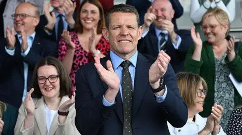 Rhun ap Iorwerth applauding on the steps of the Senedd building steps
