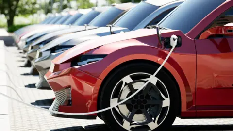 Getty Images A row of cars parked at electric charging points. The nearest car is red.