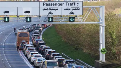 Cars and coaches queuing on road outside the Eurotunnel terminal in Folkestone with large passenger sign in foreground.