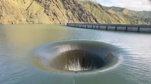 A plug-hole like effect is created on the water of a dam on a sunny day.